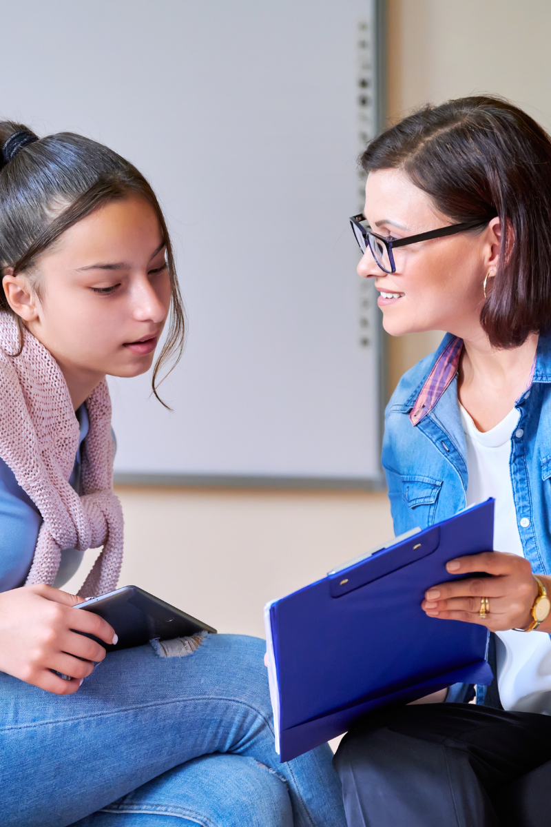 International student is speaking with a local school administrator who is holding a clipboard and listening attentively to her needs.