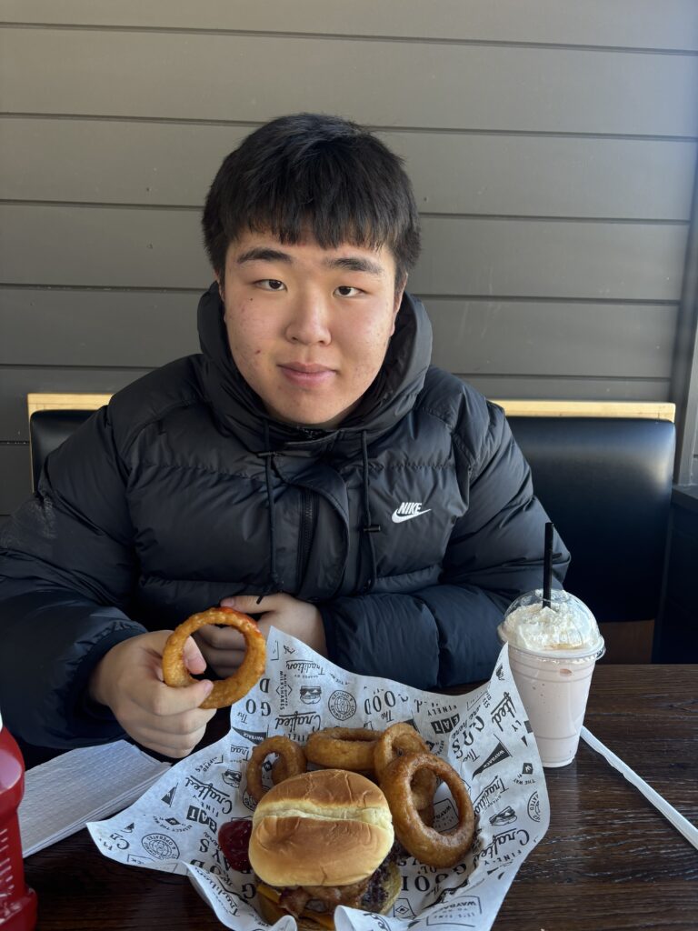 Ian smiling at a restaurant table with a burger and onion rings during his boarding school break