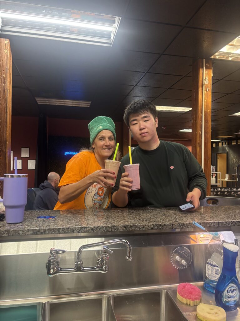 Ian holding a smoothie next to a smiling woman in a green beanie at a counter